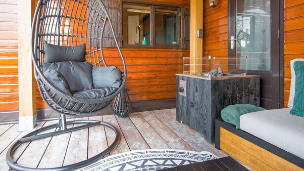 Una cabaña de madera con una silla colgante, una mesita y un sofá.