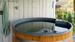 Un bain à remous en bois, surmonté d’une paroi en verre, adossé à un mur en bois, avec une serviette suspendue à proximité.