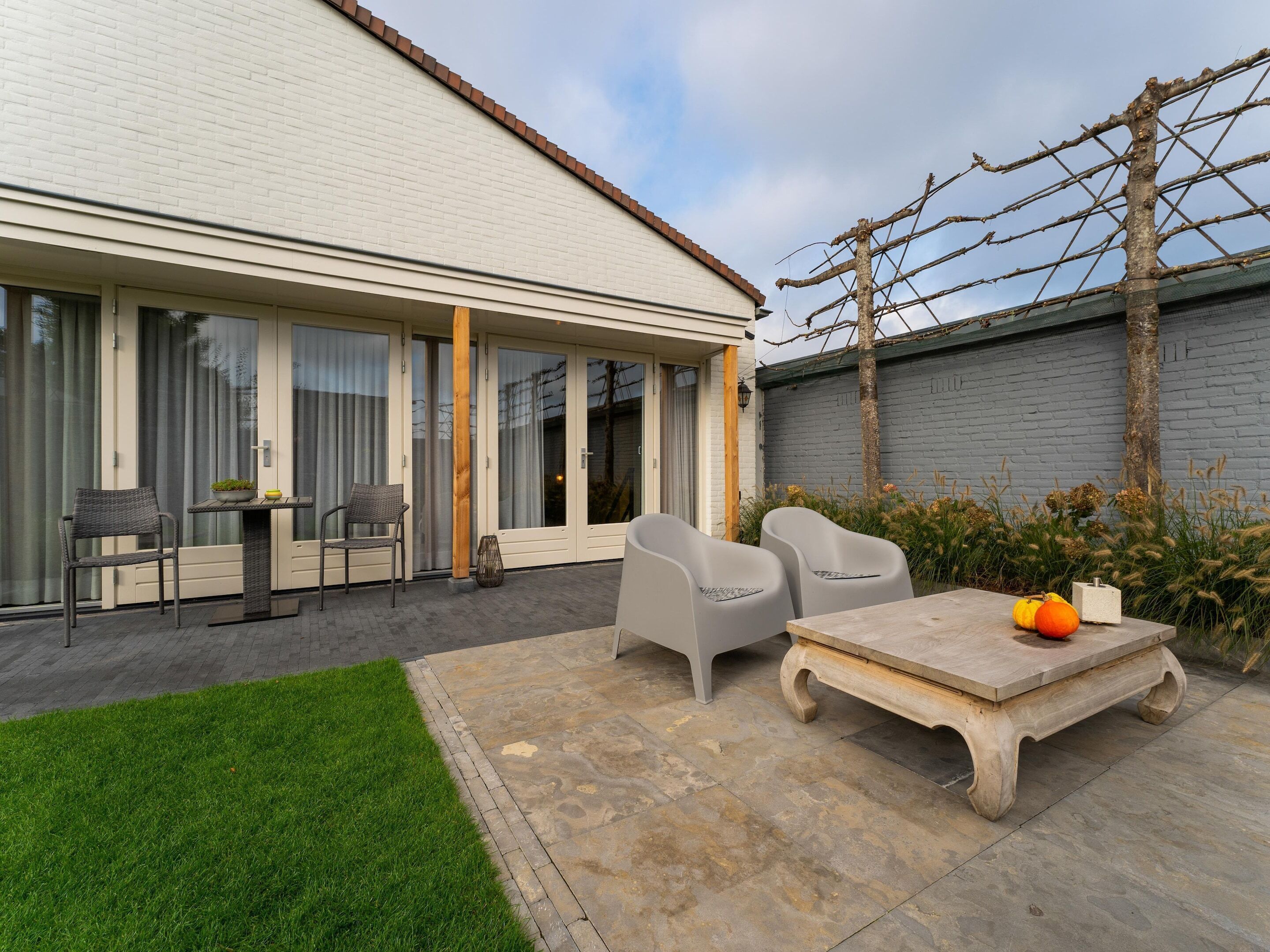 Une maison moderne dotée d’un patio comprenant une table et des chaises, un petit jardin et un mur en briques.