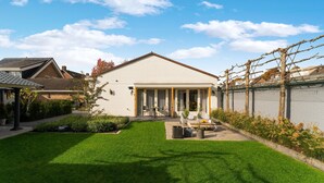 Une maison moderne avec une pelouse bien entretenue, une terrasse dotée de meubles d’extérieur et un mur de briques orné de plantes grimpantes.