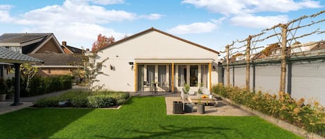 A modern house with a well-maintained lawn, a patio with outdoor furniture, and a brick wall with climbing plants.
