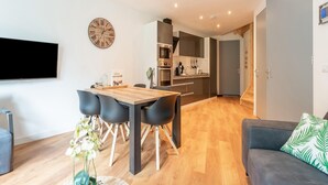 Ein modernes Wohnzimmer mit Essbereich, einer Küche und einem grauen Sofa mit grünem Blattmuster.