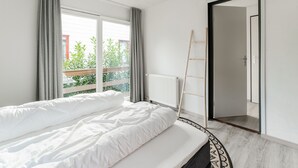 Un dormitorio con cama, un radiador, una ventana con cortinas y una puerta.