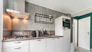 Una cocina moderna con armarios blancos, una campana extractora de acero inoxidable, un horno empotrado y un mueble de vidrio sobre el fregadero.