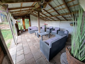 A covered patio area with wicker furniture, a stone floor, and a view of the garden. - Cozy Holiday Home in Haps (Haps)