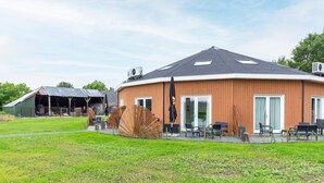 Een modern gebouw met een gebogen dak, grote ramen en terraszitplaatsen.