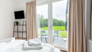 Een hotelkamer met een bed, een televisie, een plant en uitzicht op de tuin door de deur.
