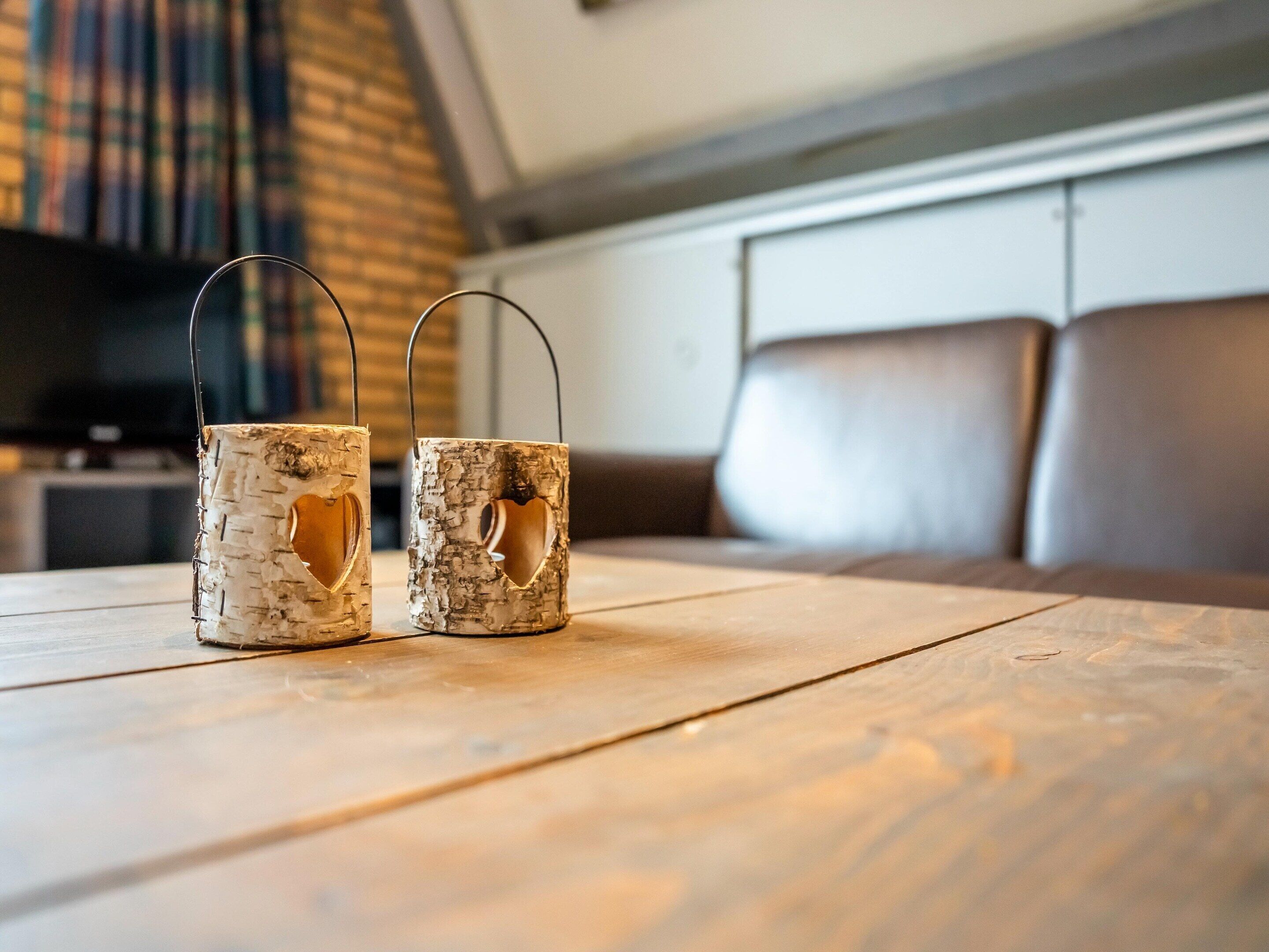 Two rustic candle holders on a wooden table in a cozy room with a brick wall and leather seating.