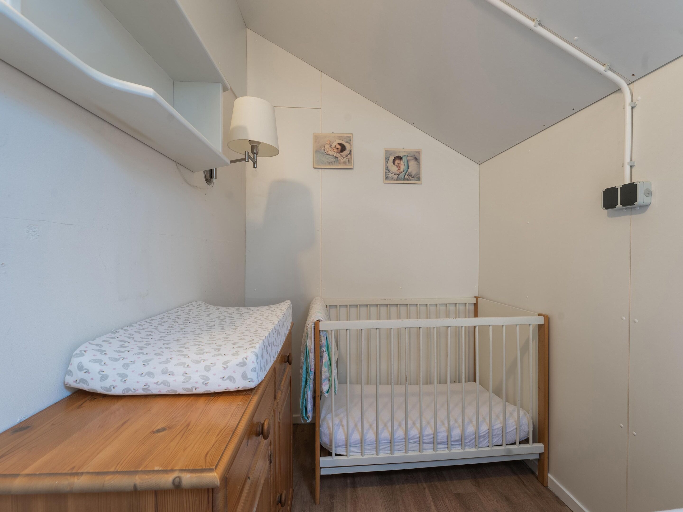 Una stanza piccola e ben illuminata con un letto di legno, una culla bianca e una lampada a parete.