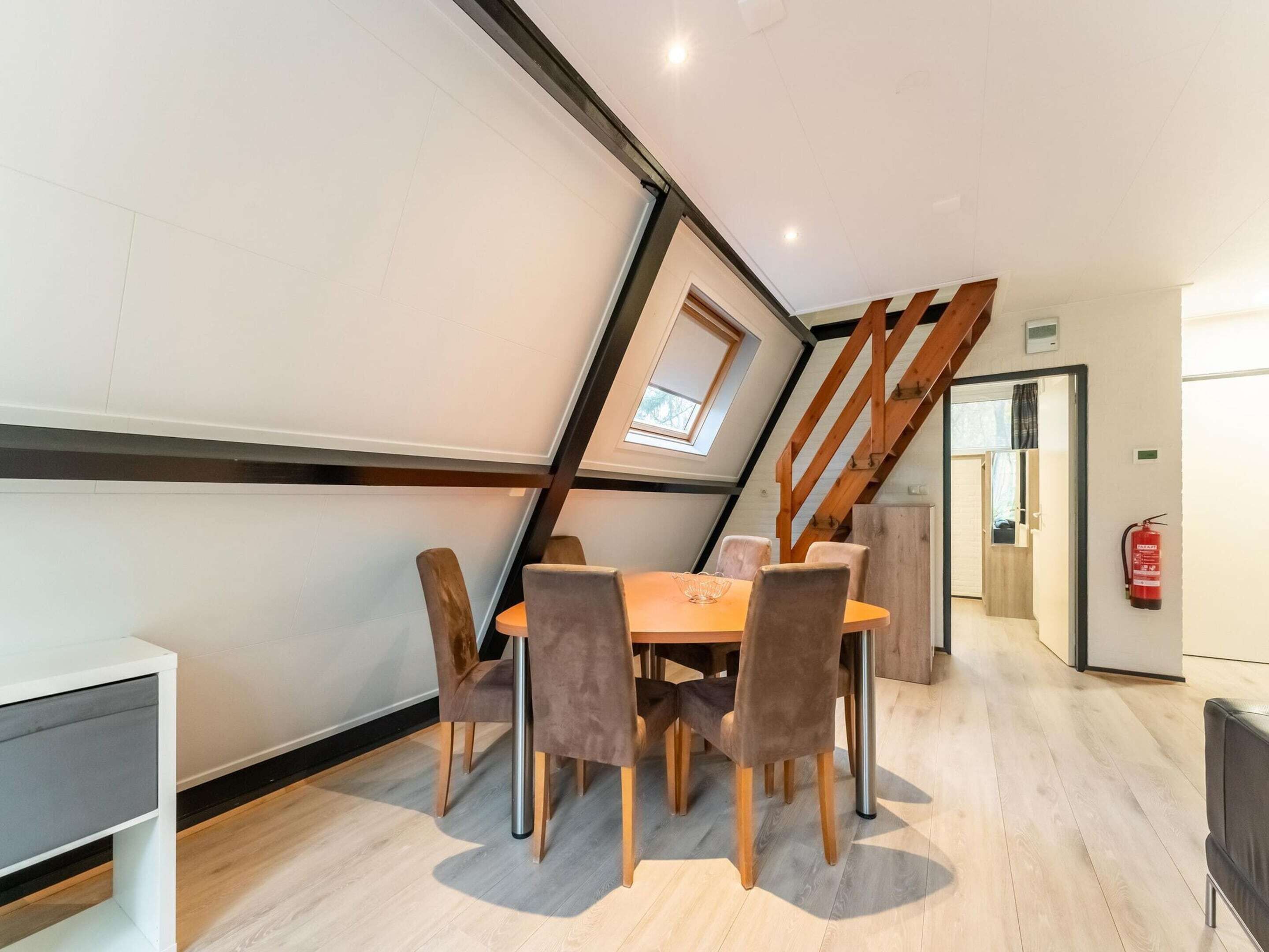 Een eethoek met een tafel en stoelen, een houten trap en een brandblusser aan de muur.