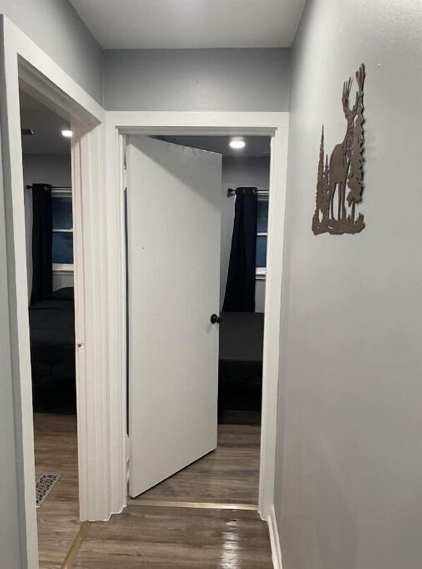 A hallway with a white door leading to a room with a bed and a black curtain.