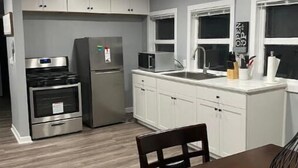 A modern kitchen with white cabinets, stainless steel appliances, and a wooden dining table. - Mankato’s Safe Haven (Mankato)