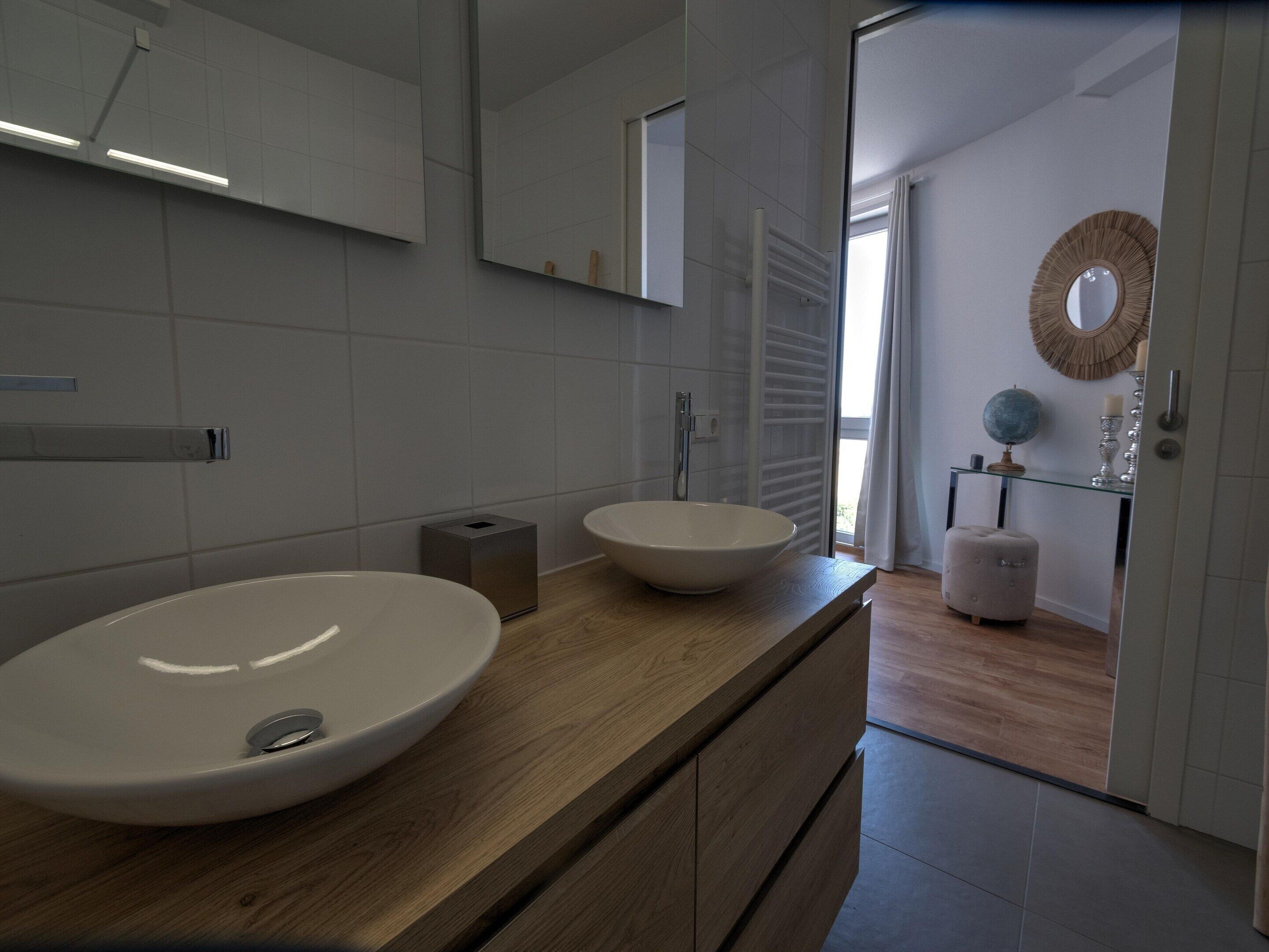 Un baño moderno con un lavabo grande, espejo y tocador de madera.