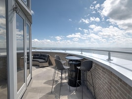 En terrasse med udsigt over havet, med et siddeområde med sofa og stole, samt et rundt bord.