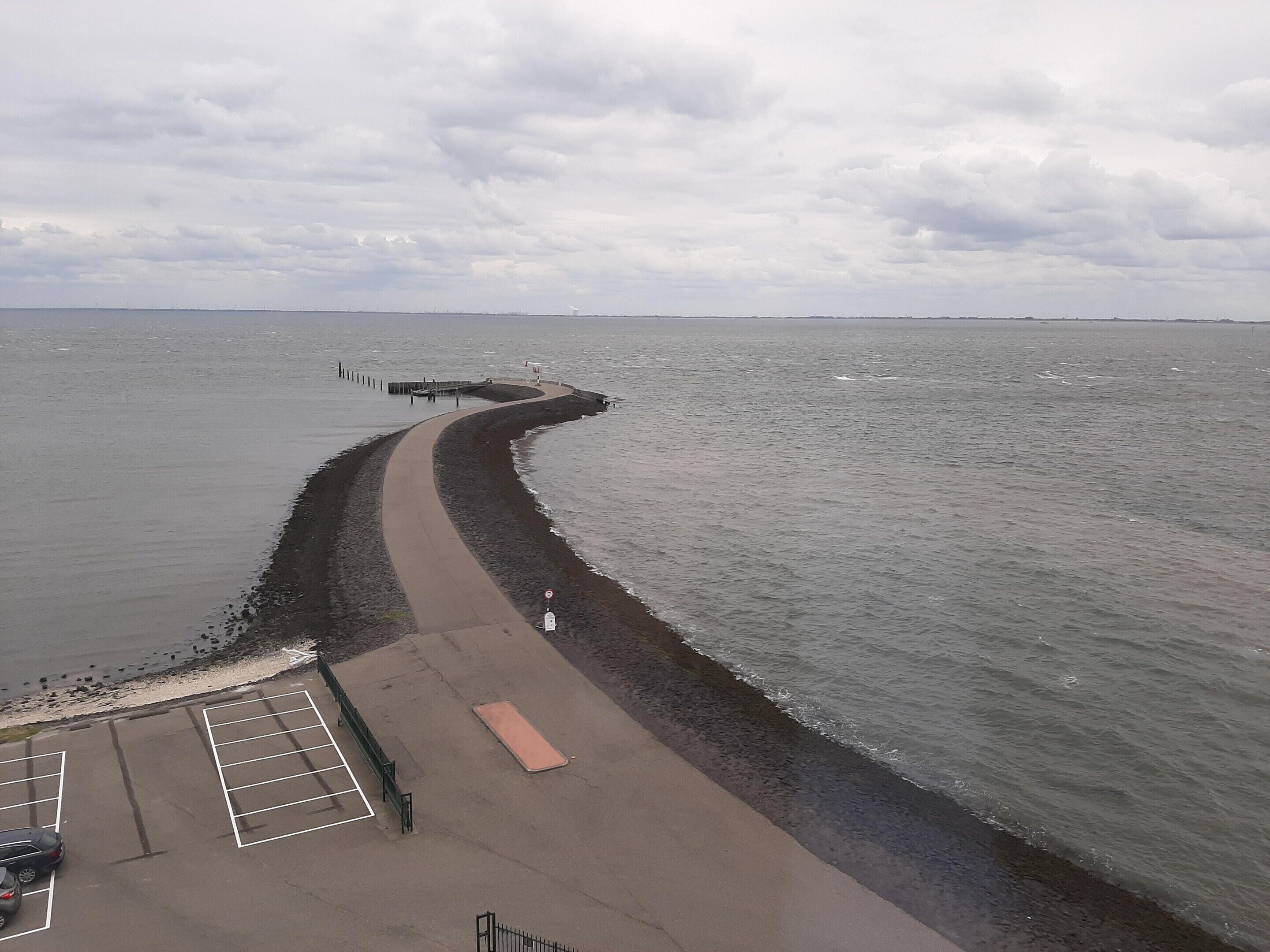 Ein Küstenweg mit einer gewundenen Wegeführung zu einem Steg, einem Parkplatz und Blick aufs Meer.