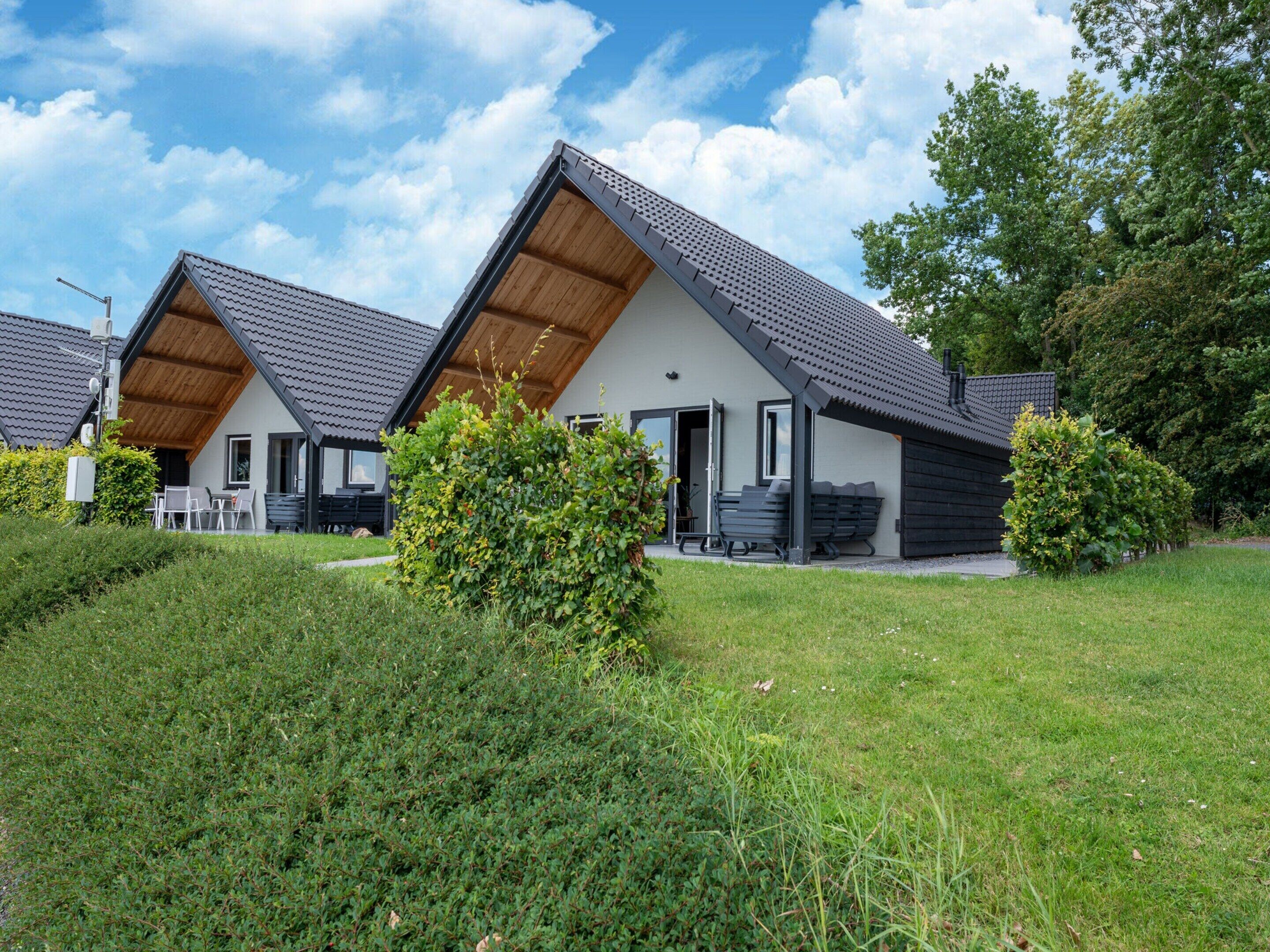 A modern, two-story residential building with a sloped roof, a covered patio, and a well-maintained lawn.
