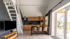 Een moderne keuken met houten kasten, een zithoek met stoelen, een televisie op een houten dressoir en een trap naar een ander niveau.