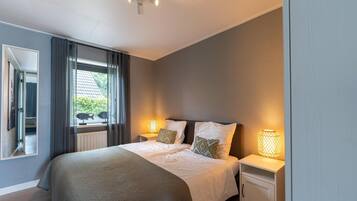 Een moderne hotelkamer met een groot bed, twee nachtkastjes met lampen, een raam met gordijnen en uitzicht op groen.