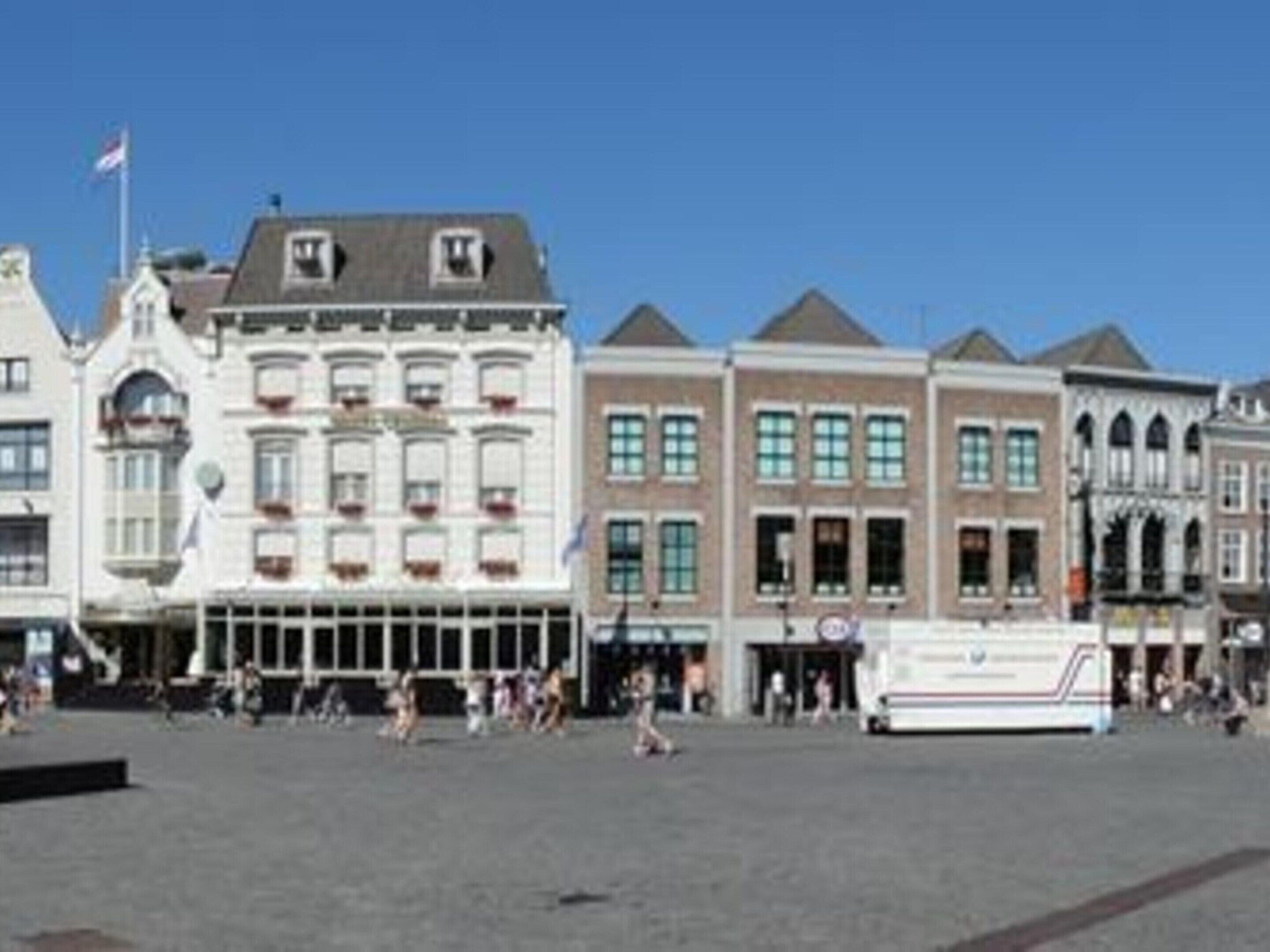 Une place bordée de bâtiments historiques, avec un drapeau et un autobus.