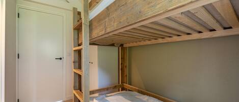 Una cama litera con estructura de madera y colchón blanco en una habitación con piso de madera y puerta blanca.