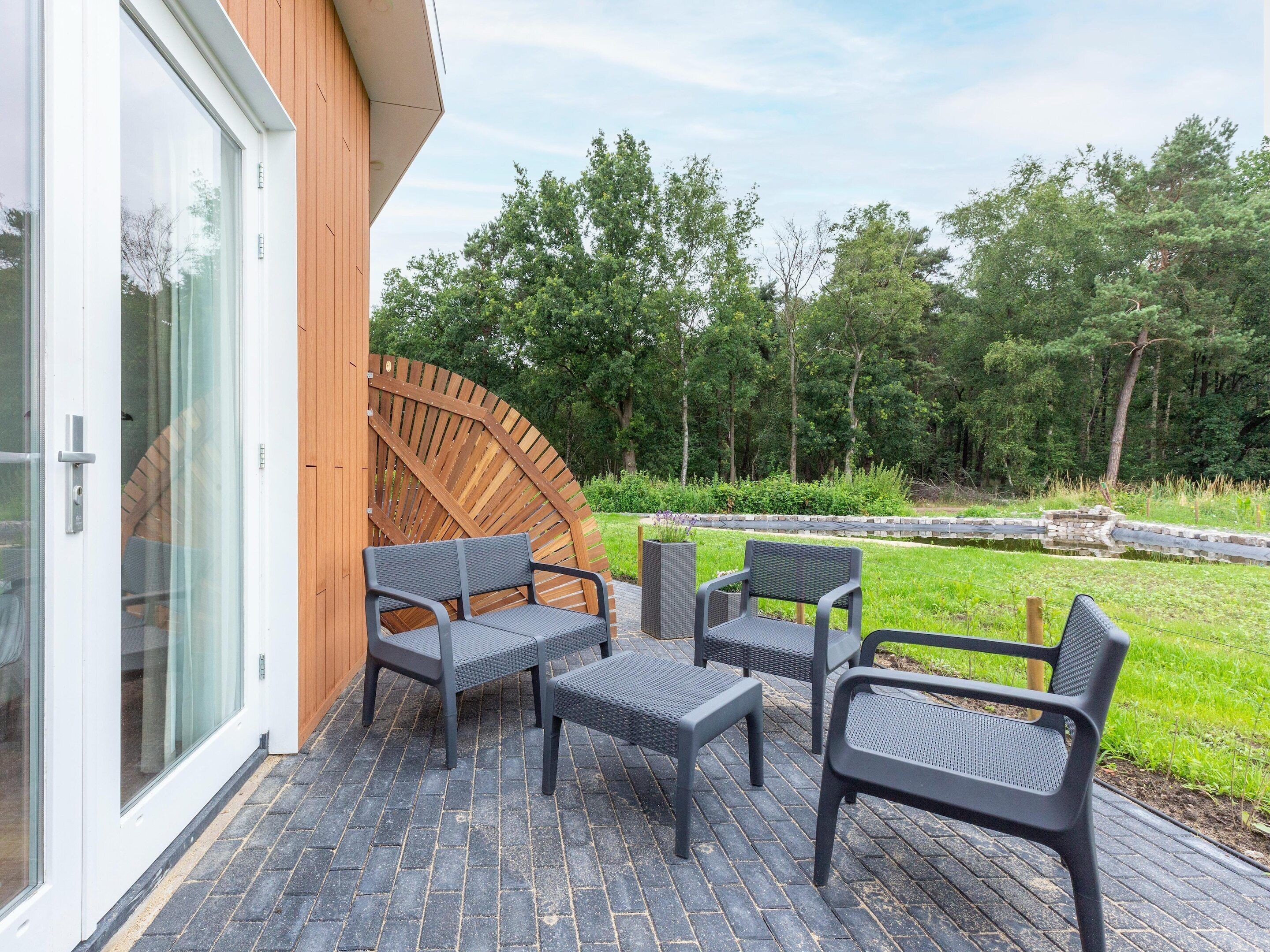 Une terrasse avec mobilier d’extérieur, une plateforme en bois et une vue sur une zone boisée.