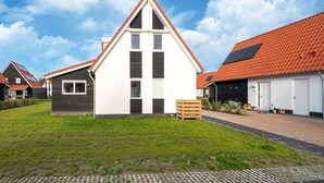 Un edificio residenziale moderno con tetto triangolare, adiacente a un garage con tetto in tegole rosse.