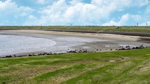 Paesaggio costiero con spiaggia sabbiosa, zone erbose e cielo sereno.
