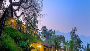 A yellow building with a balcony, surrounded by lush greenery and trees. - Gunjan Farms - Resort And Camping (Pune)