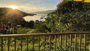 A scenic view from a balcony overlooking a lake with mountains in the background. - Gunjan Farms - Resort And Camping (Pune)