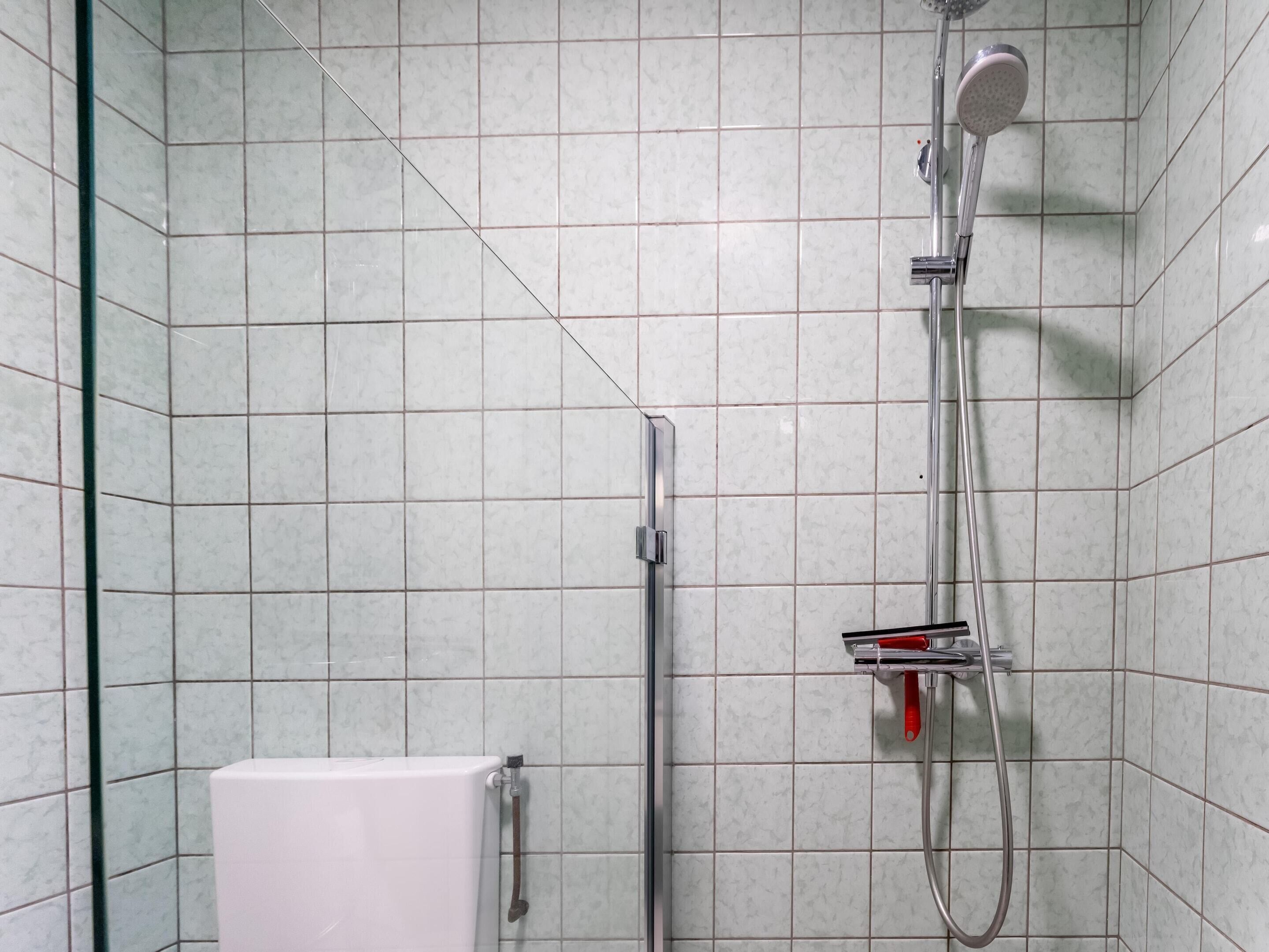 Une salle de bain moderne avec des murs recouverts de carreaux blancs, une douche en verre et des toilettes blanches.