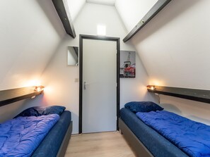 Two single beds with headboards and wall-mounted lights, a door to an adjacent room, and a framed Eiffel Tower print adorn this cozy space.