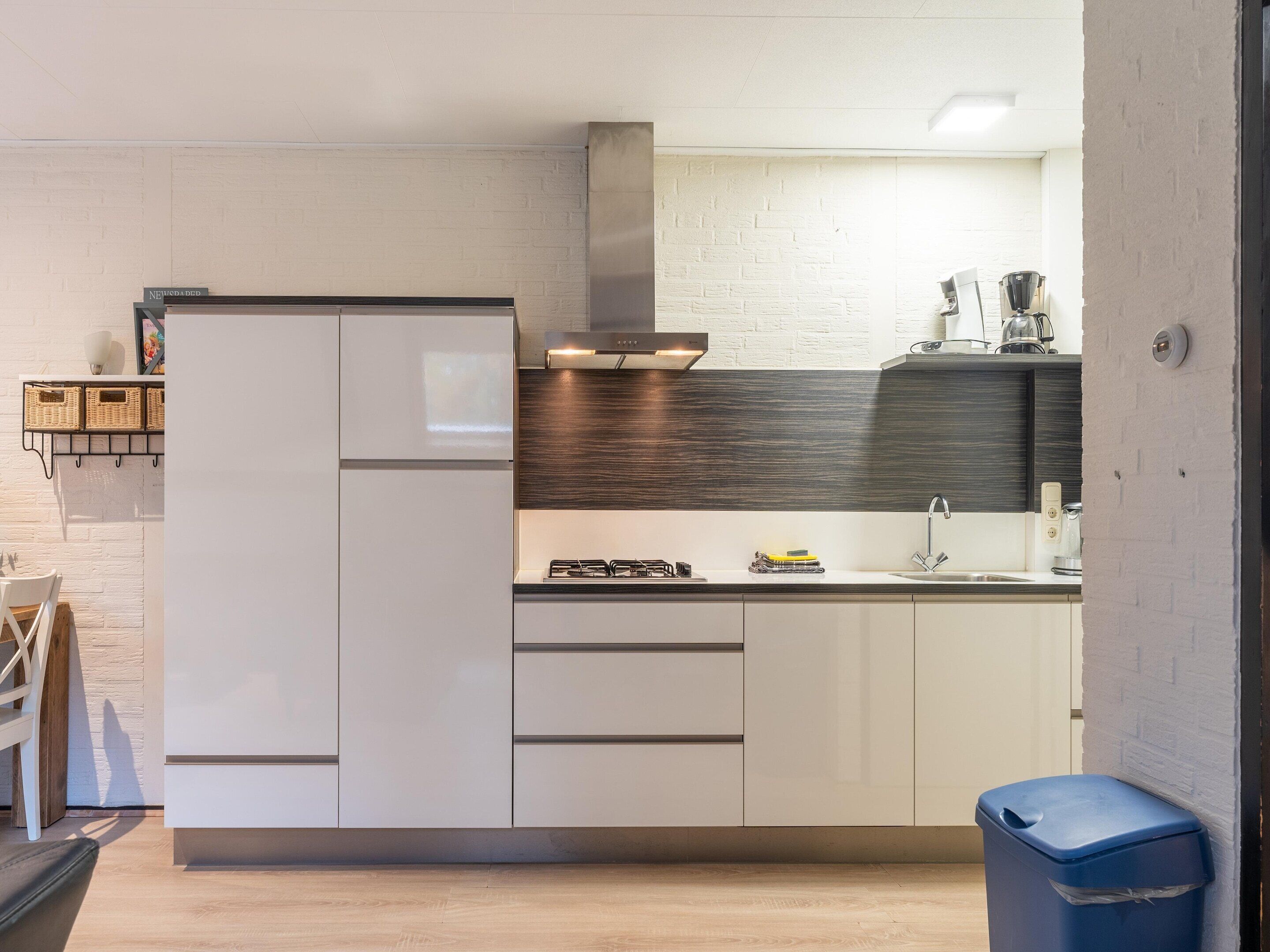 Een moderne keuken met witte kastjes, een donkere achterwand en een inbouwfornuis.