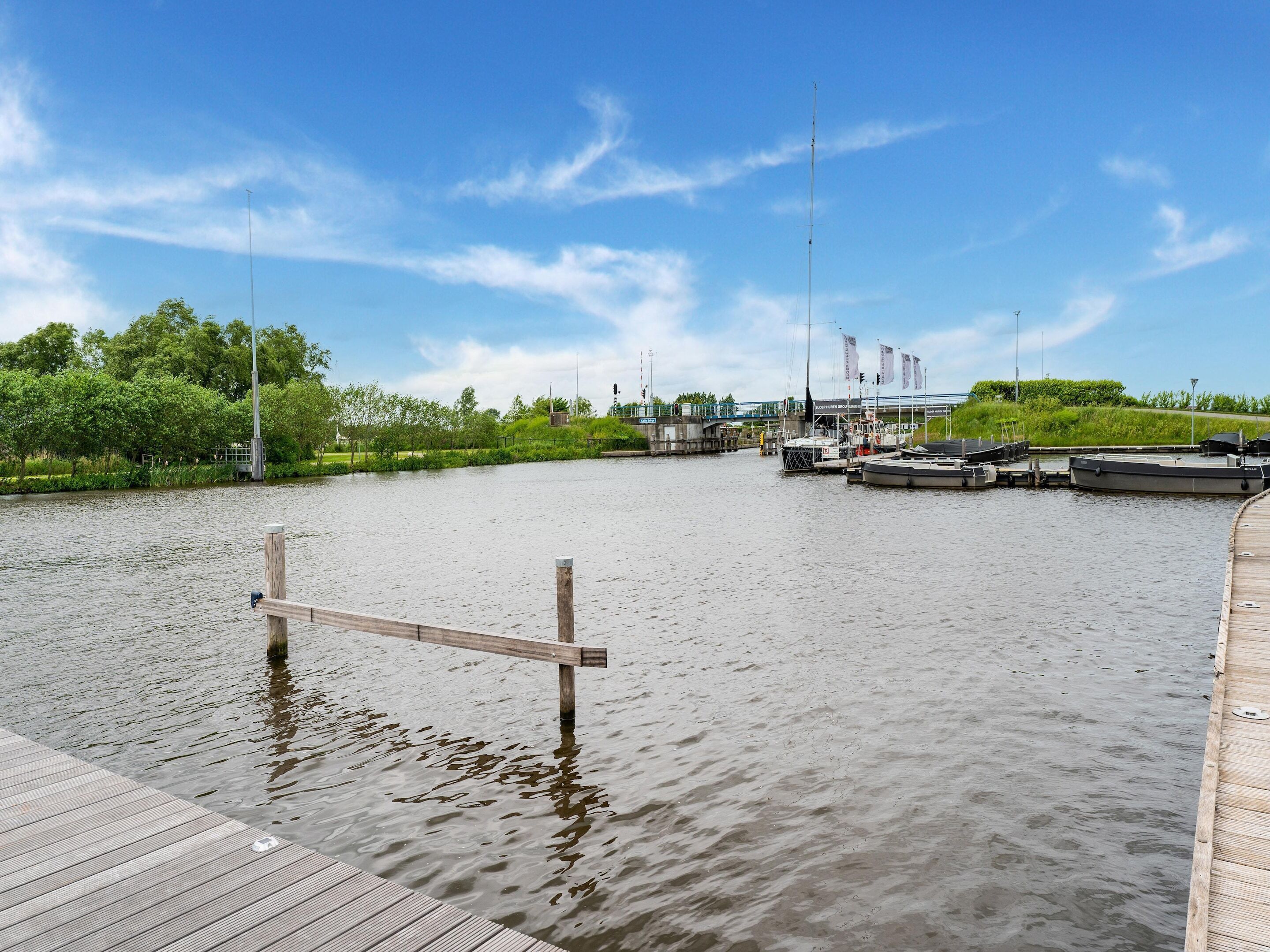 A calm river with boats docked on the right, surrounded by greenery and a clear sky.