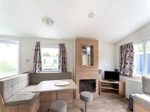 A modern, well-lit room with a sofa, a small table, a TV, and a fireplace. - Relaxing Holiday Chalet by the Water in Grou (Grou)