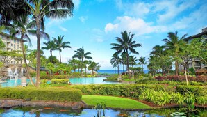 A resort with a swimming pool, a small pond with fish, palm trees, and a view of the ocean.