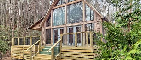 A cabin with a wooden exterior, large windows, and a wooden staircase leading to a deck.