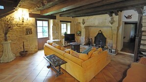 A rustic living room with a stone fireplace, a sofa, a television, and a stone wall. - Authentic 19th c Farmhouse  with heated pool fiber optic and air conditionné (Saint-Germain-des-Prés)