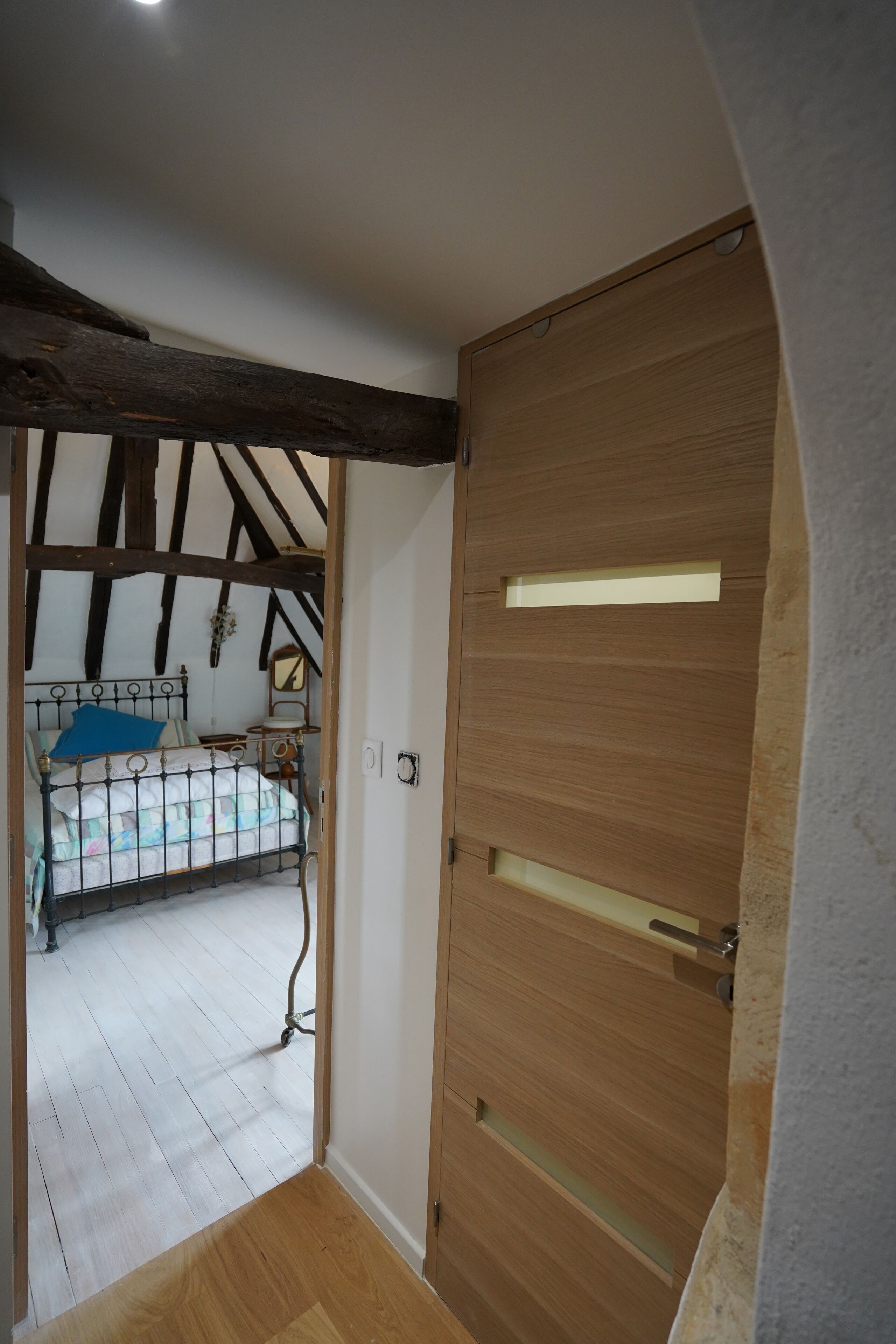 Una habitación con puerta de madera, una cama con almohada azul y techo de madera con vigas a la vista.