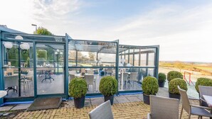 A glass-enclosed patio area with wicker furniture and potted plants. - Beautiful Holiday Home in Voerendaal (Voerendaal)