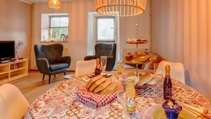 A cozy living room with a round table set for a meal, featuring bread, wine, and a dessert. Two chairs are positioned around the table, and a television is visible in the background. - Beautiful Holiday Home in Voerendaal (Voerendaal)