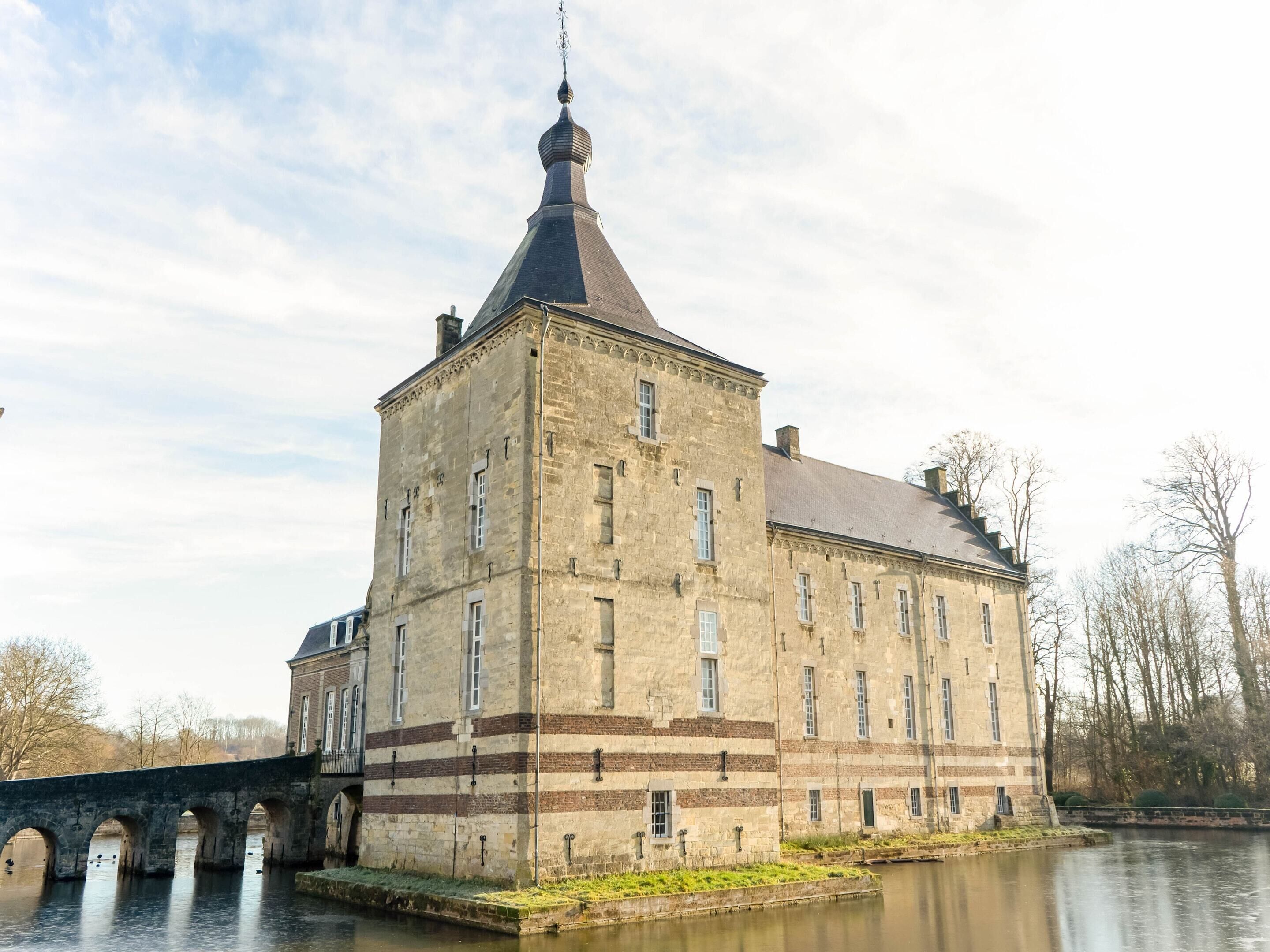 Een historisch stenen gebouw met een opvallende toren en een brug op de achtergrond.
