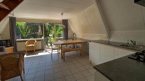 Cozinha espaçosa com área de refeições, grandes janelas e vista para o verde.