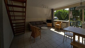 Sala de estar com sofá, uma poltrona de vime, televisão e mesa de jantar com cadeiras.