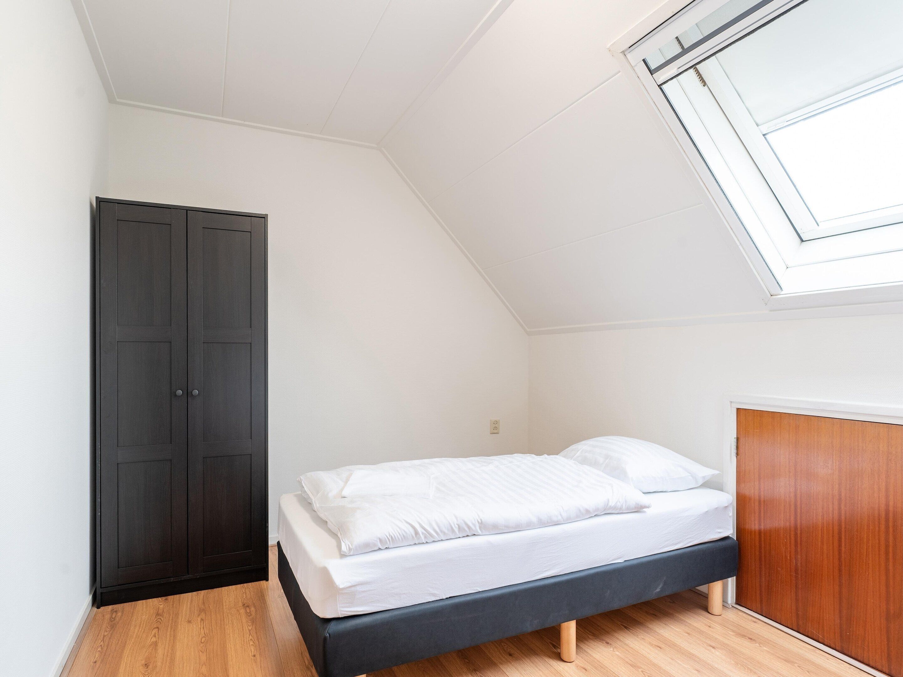 A bedroom with a bed, a wardrobe, and a skylight.