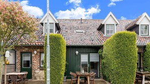 A traditional building with a tiled roof, brick walls, and a green door. There is a table and chairs outside, and a hedge in front. - Cottage in Ubachsberg With Scenic Hills (Voerendaal)