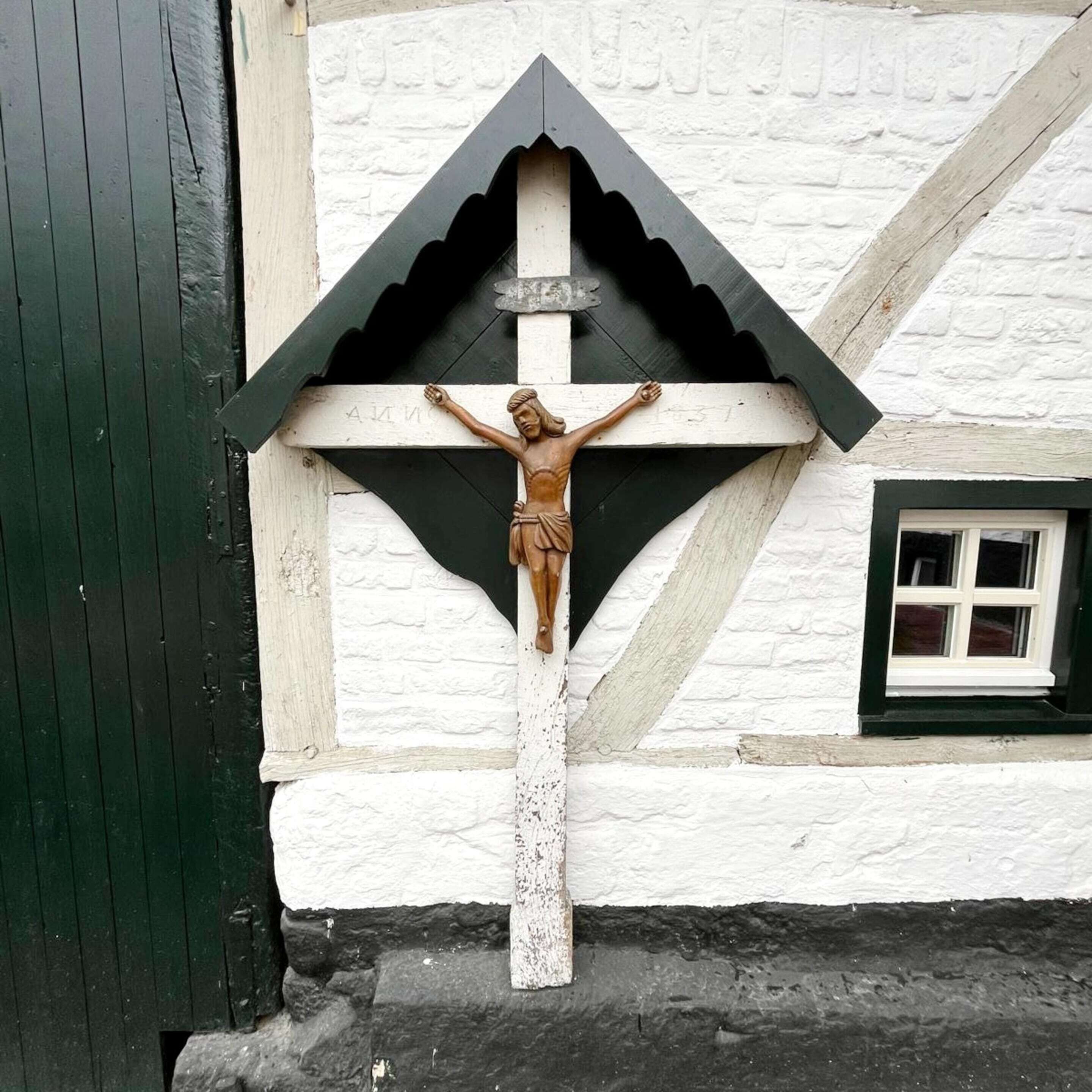A wooden crucifix mounted on a white wall with a black triangular frame.