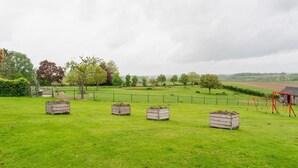 A grassy field with wooden planters, a fenced area, and a red swing set. - Cottage in Ubachsberg With Scenic Hills (Voerendaal)