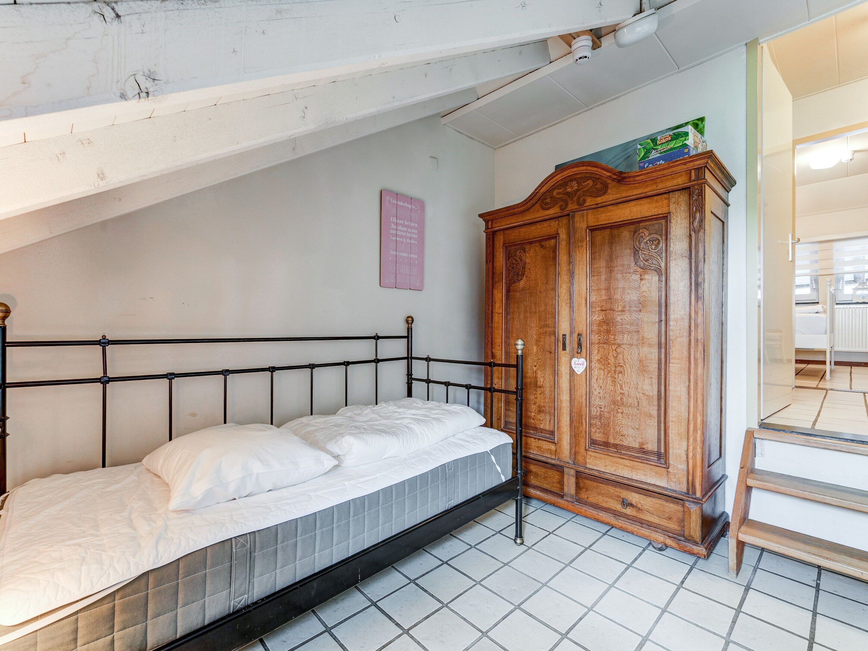 A single bed with a headboard, a wooden wardrobe, and a small shelf with items on top.