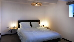A neatly made bed with white linens, two bedside tables with lamps, and a modern chandelier. - Attractive Apartment in South Limburg (Klimmen)