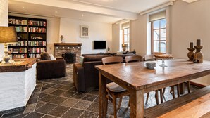 A spacious living room with a fireplace, a large bookshelf, and a dining area with a wooden table and benches. - Holiday Home in South Limburg With a Terrace (Klimmen)